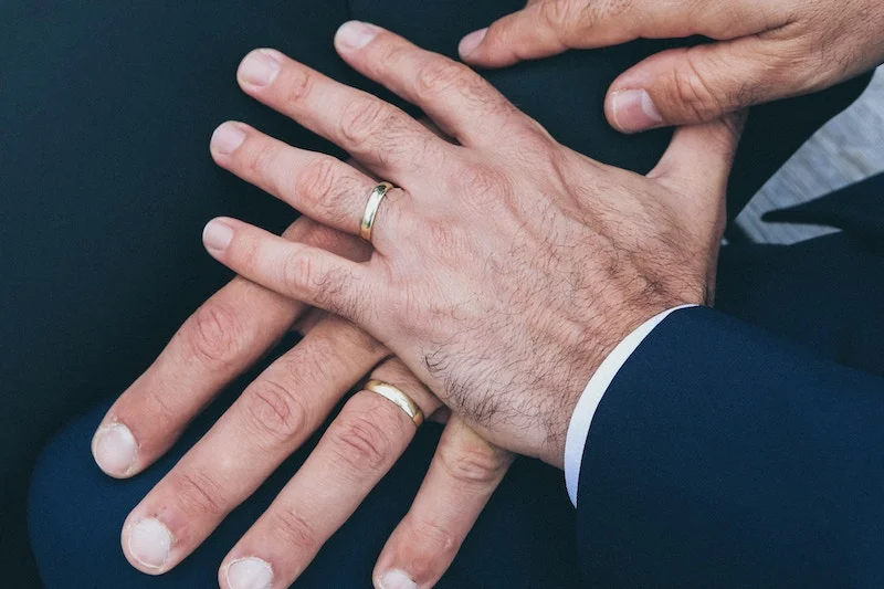 Two men's hands holding each other's wedding rings with long island wedding officiants.