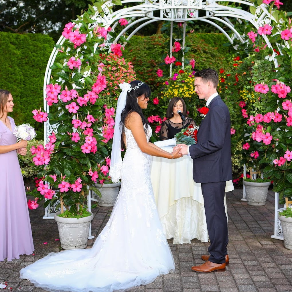 A bride and groom, accompanied by a wedding officiant from Long Island, exchange vows in front of a beautiful flower garden.
