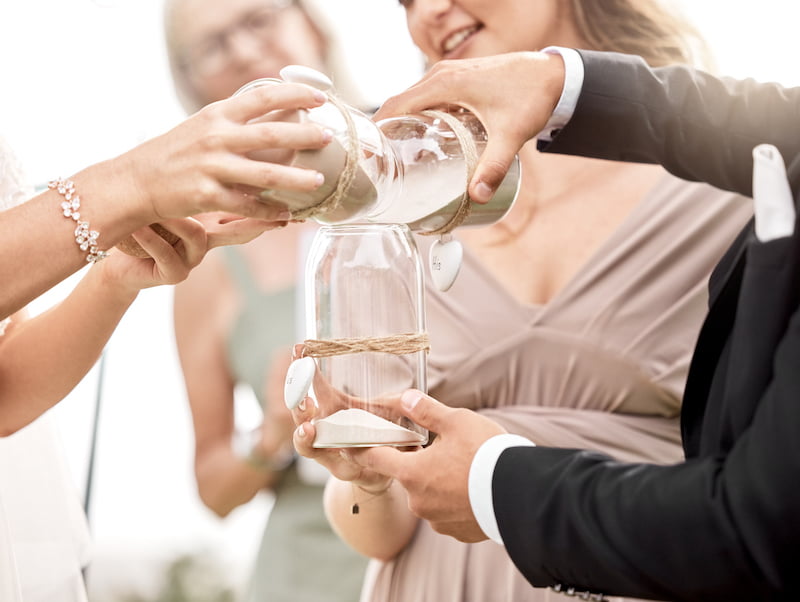 A group of people, including a long island wedding officiant, pouring sand into a jar.