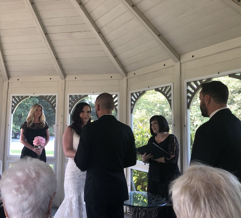 A bride and groom, accompanied by a Long Island wedding officiant, exchange vows in a gazebo.