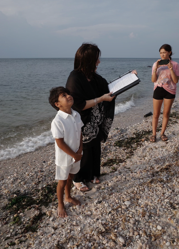 A woman holding a book next to a child on the beach, officiated by long island wedding officiants.